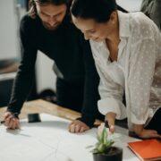 man and woman leaning on table staring at white board on top of table having a meeting