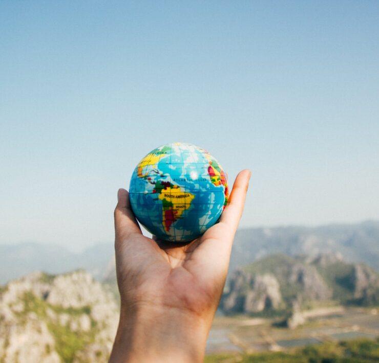 person holding world globe facing mountain