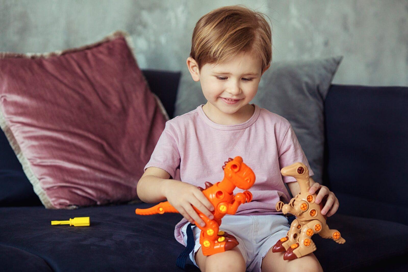 cute boy sitting on a sofa playing with his dinosaur toys