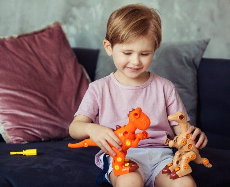 cute boy sitting on a sofa playing with his dinosaur toys