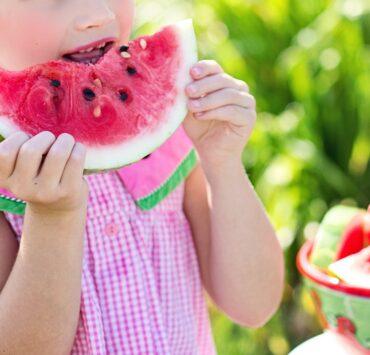 girl eating sliced watermelon fruit beside table