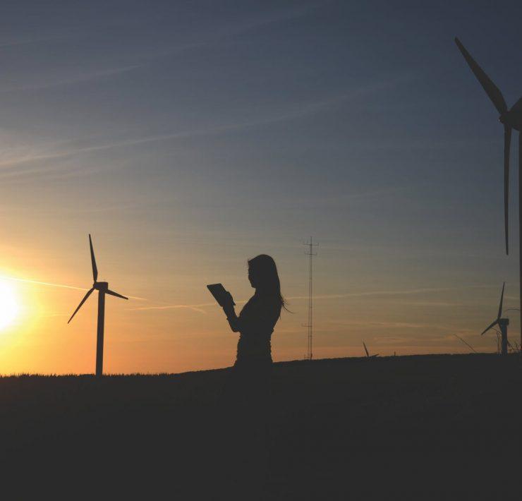 silhouette of woman holding book near windmills