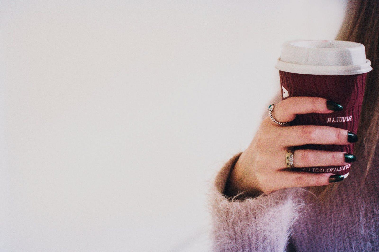 person with black manicured nails holding brown cup with white lid