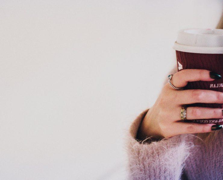 person with black manicured nails holding brown cup with white lid
