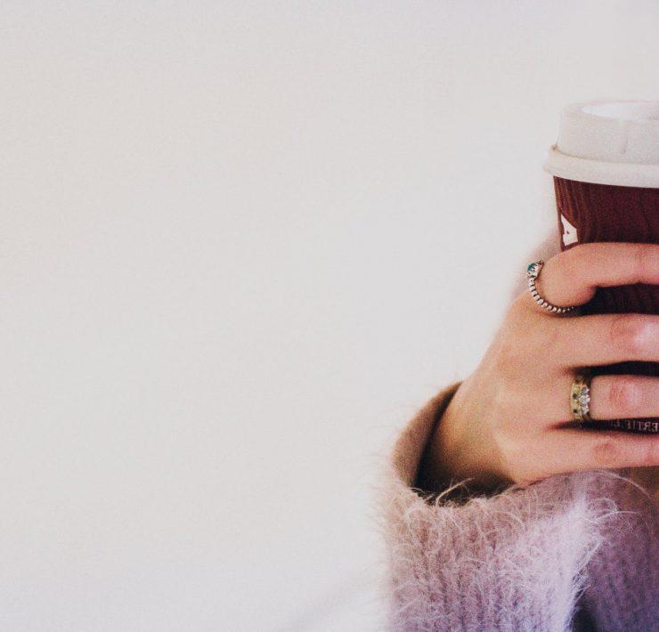 person with black manicured nails holding brown cup with white lid