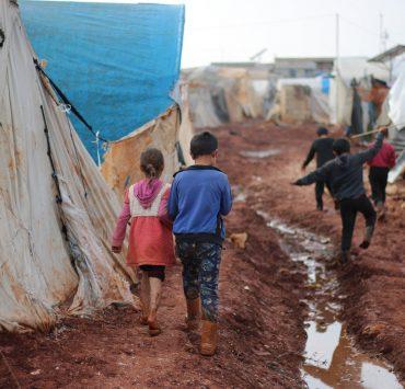 children walking on dirty street with tents