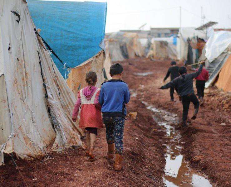 children walking on dirty street with tents