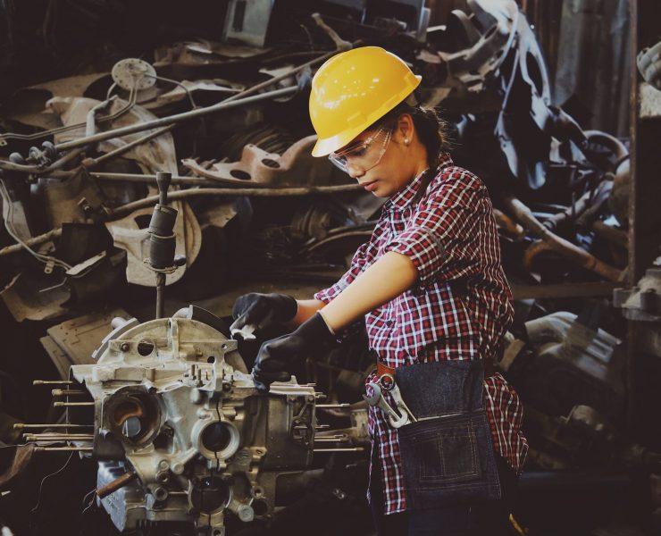 woman wears yellow hard hat holding vehicle part