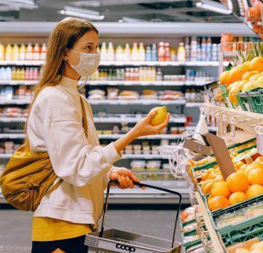 woman in yellow tshirt and beige jacket holding a fruit stand