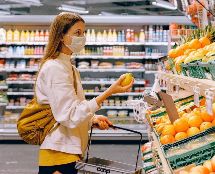 woman in yellow tshirt and beige jacket holding a fruit stand