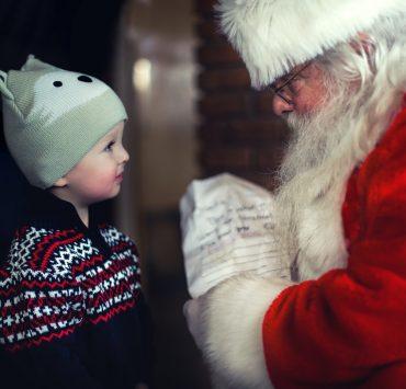 toddler in black sweater standing in front of Santa Claus