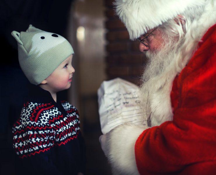 toddler in black sweater standing in front of Santa Claus