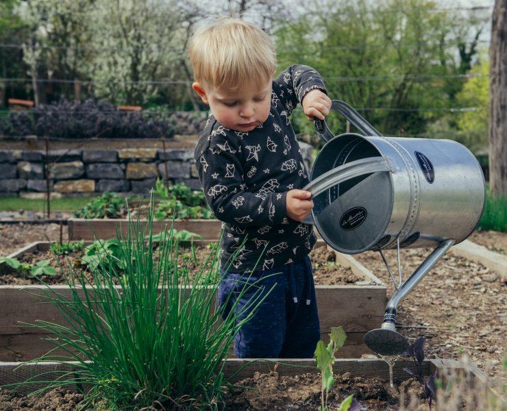boy in black and white long sleeve shirt standing beside gray metal watering can during daytime