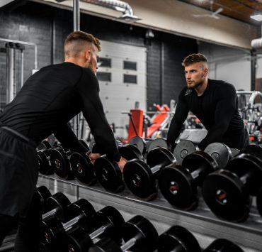 man in black long sleeve shirt and black pants carrying black dumbbell