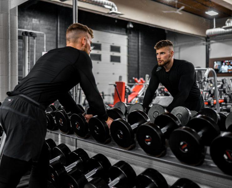 man in black long sleeve shirt and black pants carrying black dumbbell