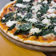 pizza with green leaves on brown wooden table