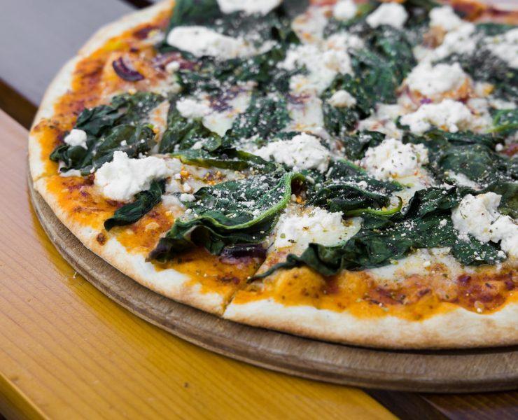 pizza with green leaves on brown wooden table