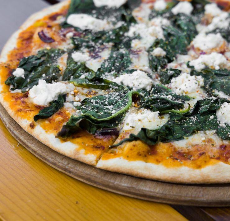pizza with green leaves on brown wooden table