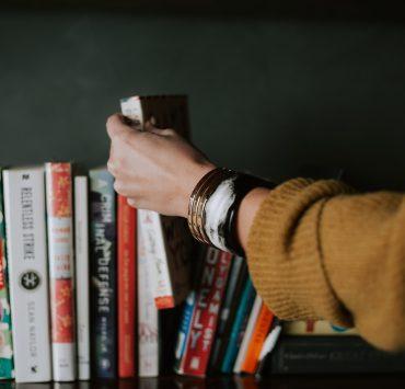 person picking white and red book on bookshelf