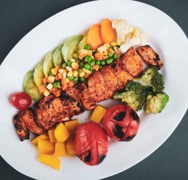 grilled meat with sliced lemon and sliced tomatoes on white ceramic plate