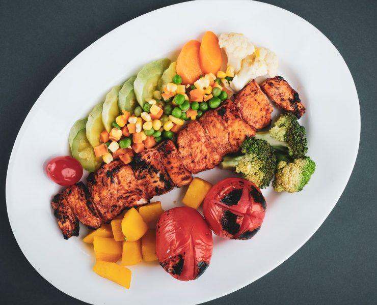 grilled meat with sliced lemon and sliced tomatoes on white ceramic plate