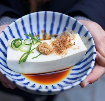 person holding white and blue ceramic plate with rice and sliced cucumber