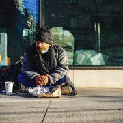 man in black and gray jacket sitting on sidewalk during daytime