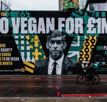a man riding a bike past a large mural of a man in a suit