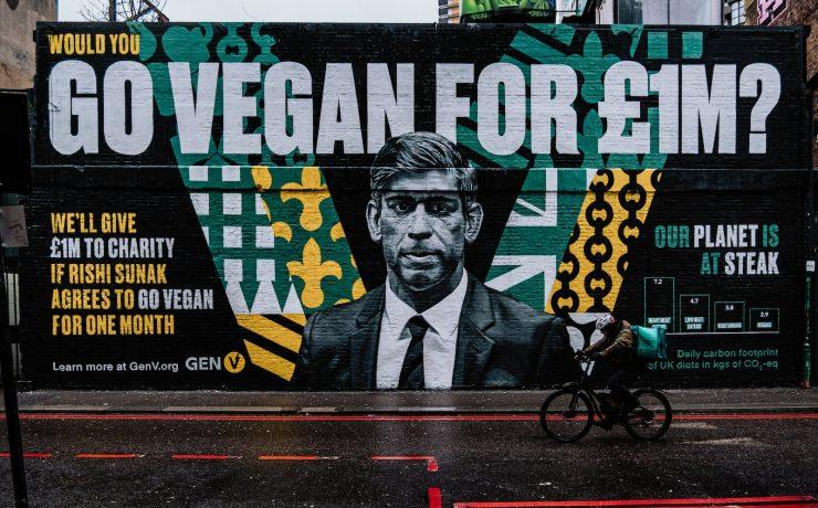 a man riding a bike past a large mural of a man in a suit