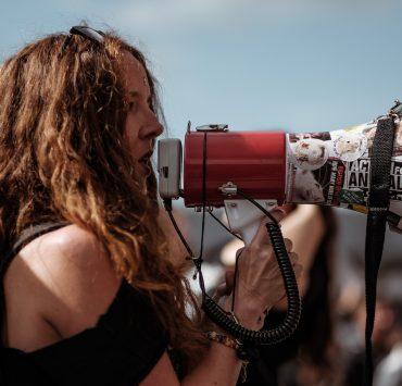 selective focus photography of woman wearing black cold-shoulder shirt using megaphone during daytime