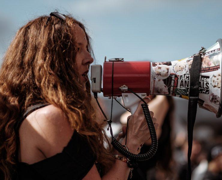 selective focus photography of woman wearing black cold-shoulder shirt using megaphone during daytime