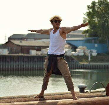 man in white tank top and brown pants jumping on brown wooden dock during daytime