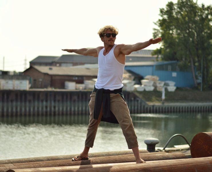 man in white tank top and brown pants jumping on brown wooden dock during daytime