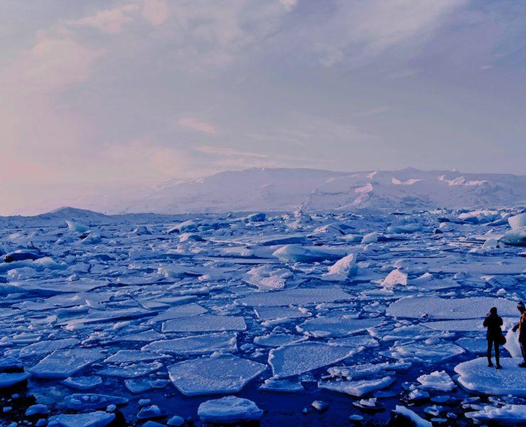 man and woman standing cracked sea ice under gray sky