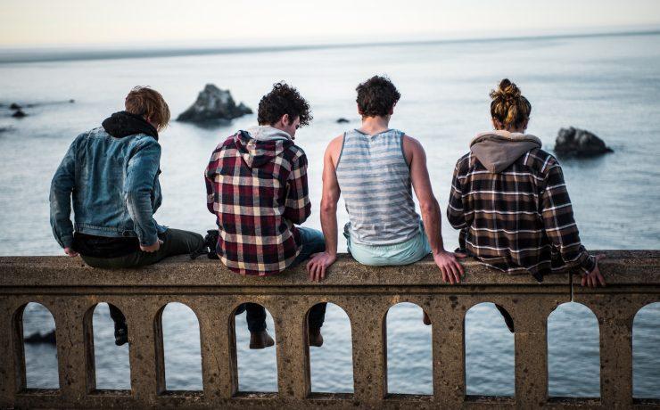 four person sitting on bench in front of body of water