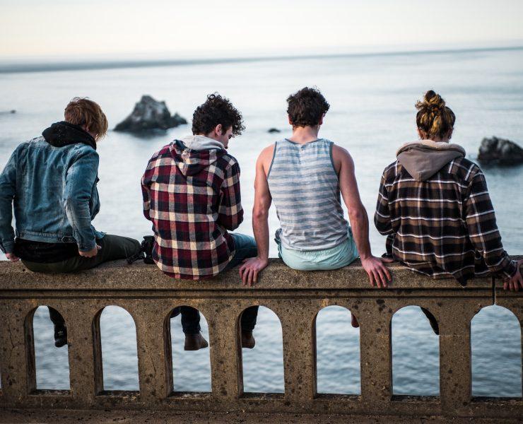 four person sitting on bench in front of body of water