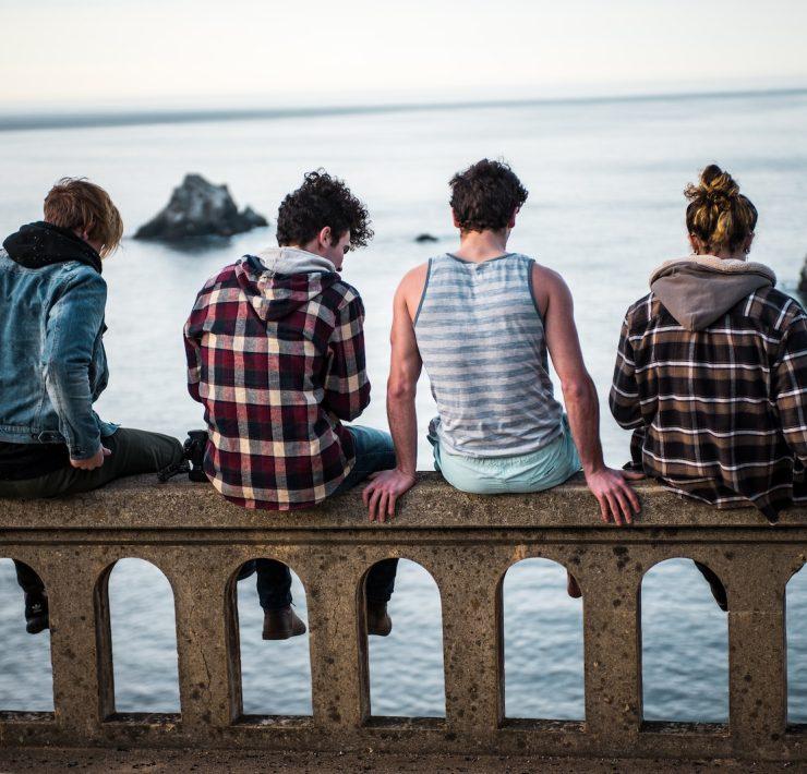 four person sitting on bench in front of body of water