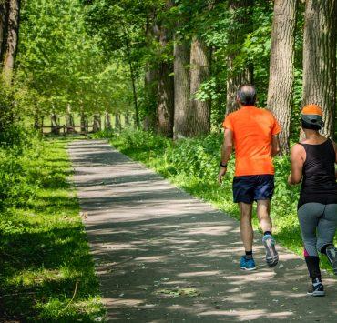 man in orange t-shirt and gray pants with blue shoes walking on pathway