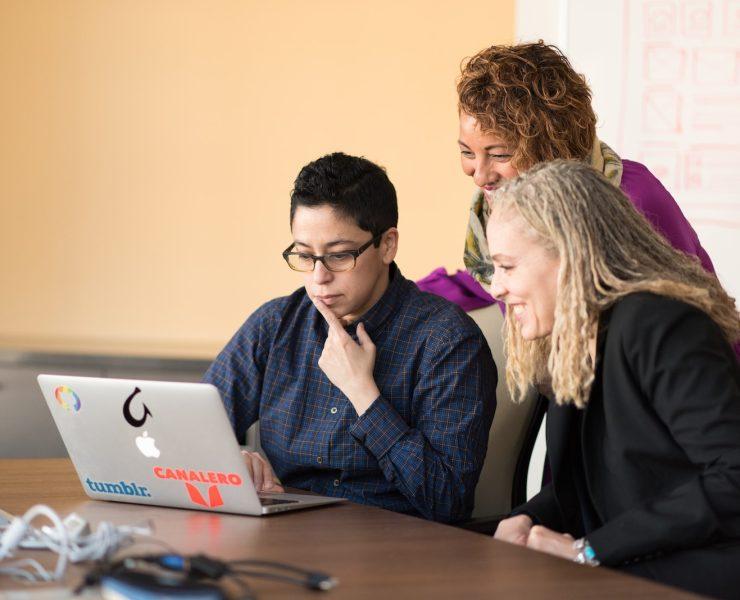 three women beside table looking at MacBook