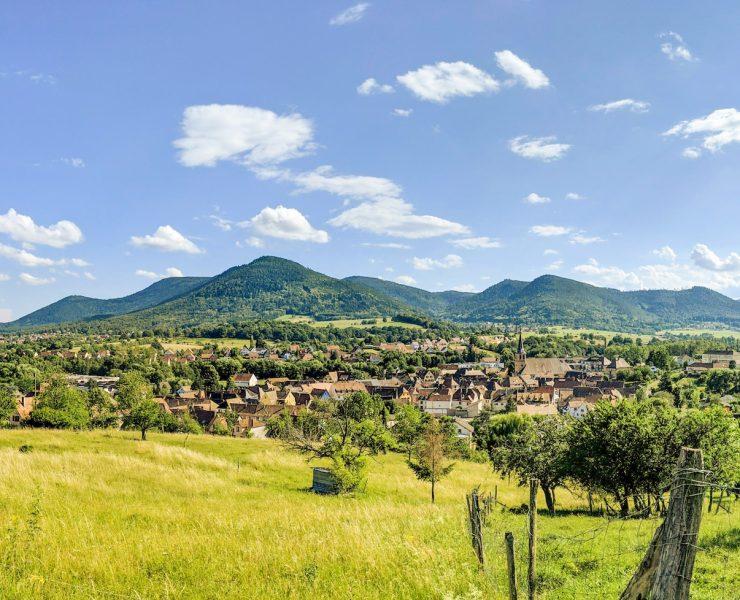 green grass field near green mountain under blue sky during daytime