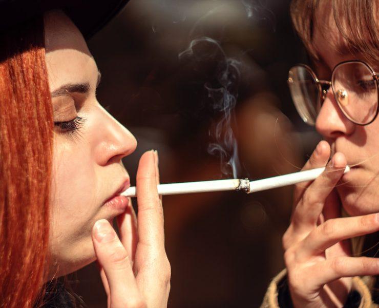 two women smoking a cigarette and looking at each other