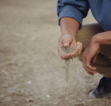 Person crouches down with a handful of sand that slips through their fingers