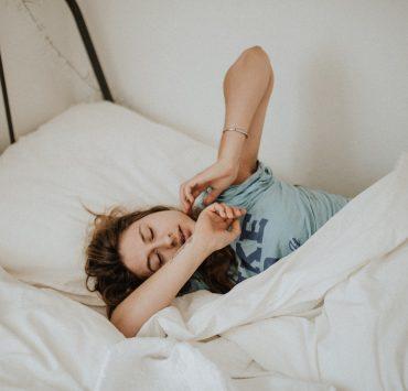 woman covered in white blanket sleeping on white bed comforter