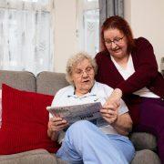 a woman sitting on a couch next to a woman reading a newspaper