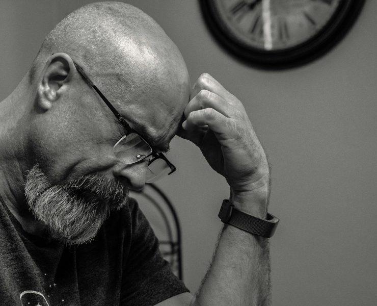 Grayscale Photo of Man Thinking in Front of Analog Wall Clock