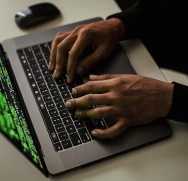 From above of crop anonymous male hacker typing on netbook with data on screen while sitting at desk